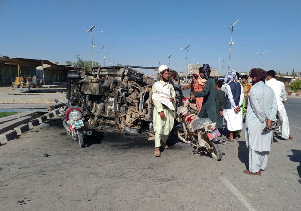 Afghans stand near a burnt car inside the city of Farah, capital of Farah province, southwest Afghanistan